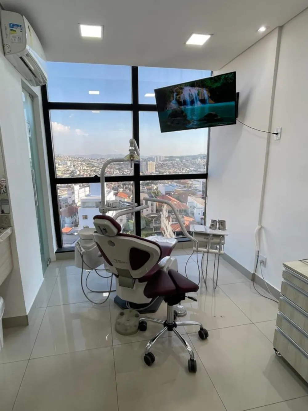 Foto do consultório da Karine Sayure, mostrando uma bela vista, uma televisão e cadeira de dentista