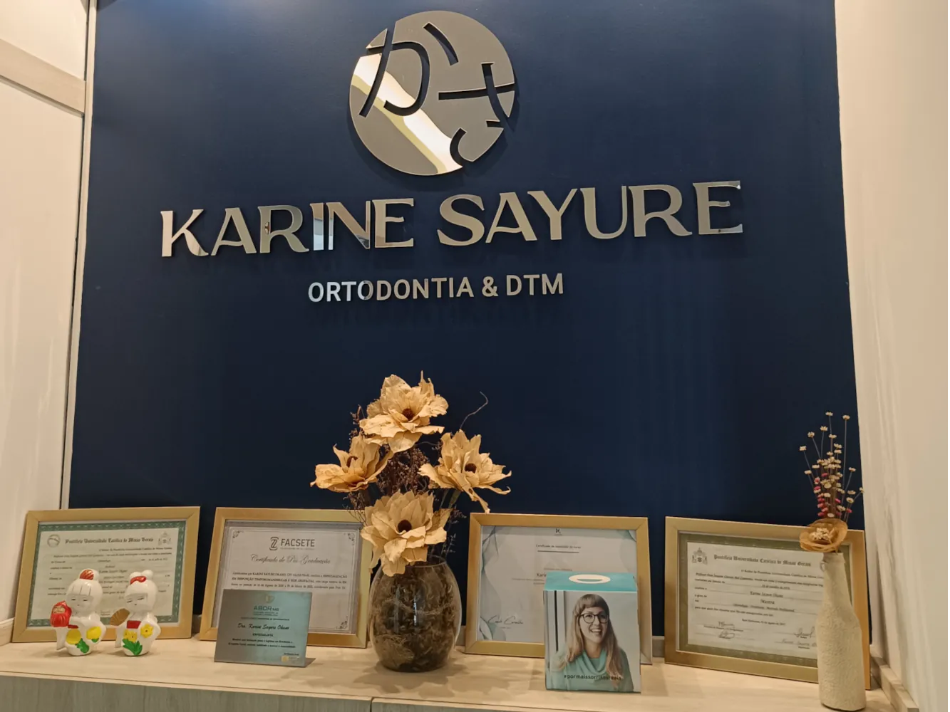 foto dobalcão do consultório da Karine Sayure com a placa de ortodontia e DTM e seus certificados