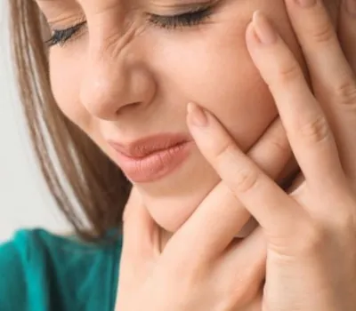 Mulher branca com feição de dor na boca com as mãos na mandibula